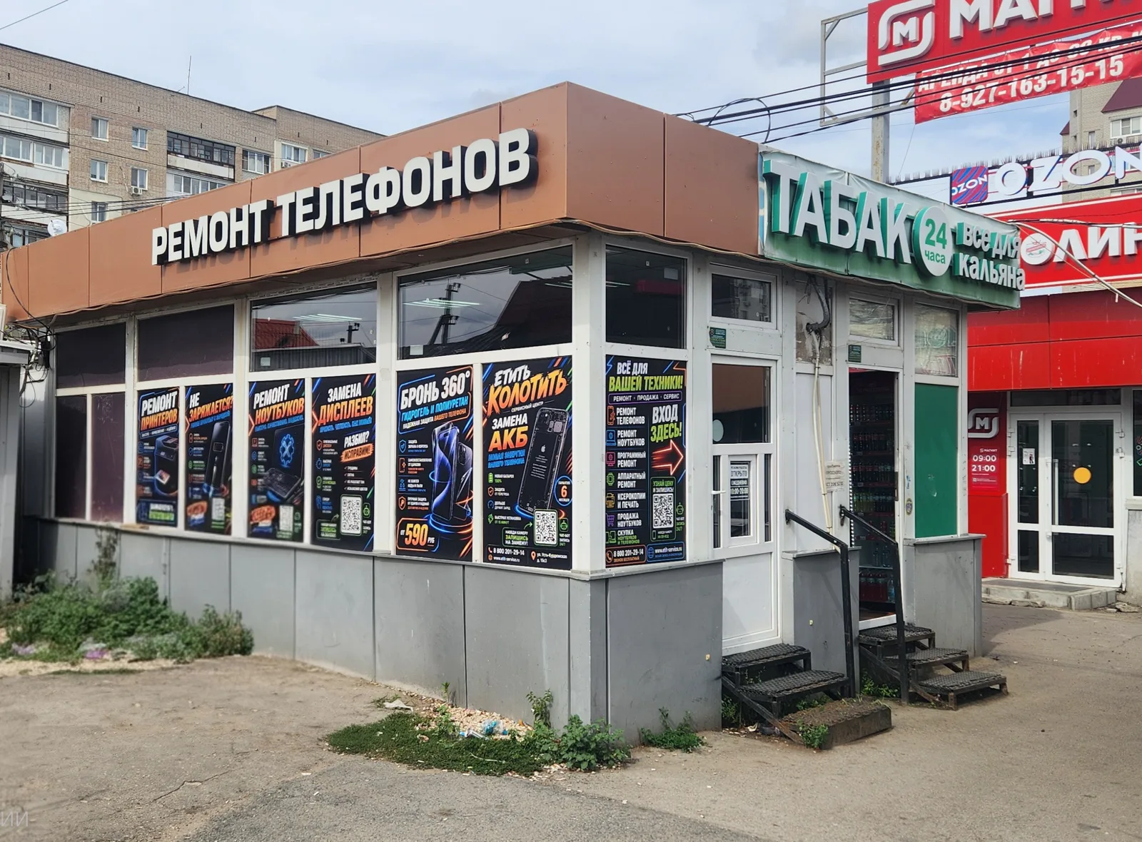 Павильон сервисного центра «Етить Колотить» на остановке: вывеска «Ремонт телефонов» и баннеры на витрине